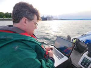 Robert Dall working on his laptop from a boat in the middle of Commencement Bay in Tacoma, Washington.