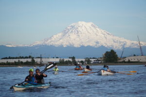 Team from the Seventy48 race kayaking on Commencement Bay with Mount Rainier in the background.